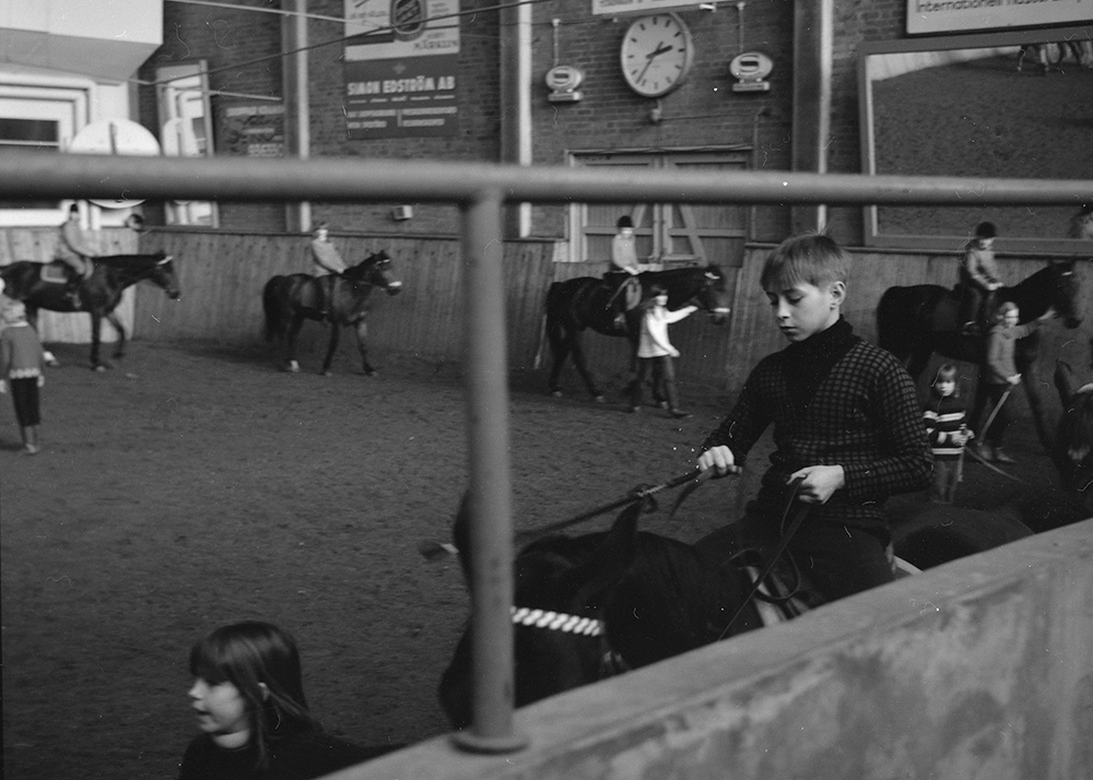 Äldre svartvitt fotografi. Barn rider på hästar i en manege.