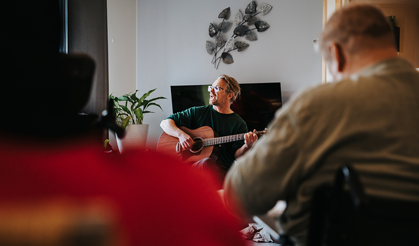 Gustaf spelar gitarr. Han har blont hår och glasögon.