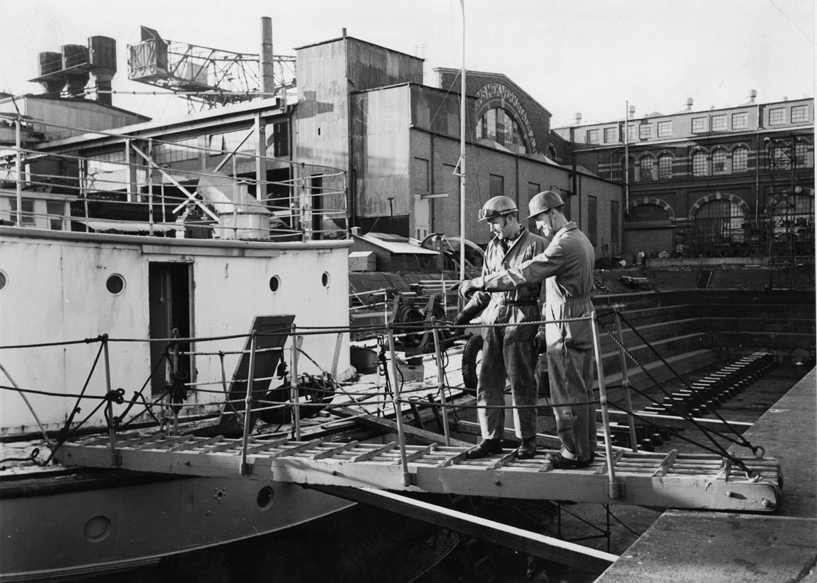 Två män som inspekterar ett mindre fartyg i Malmös äldsta torrdocka, 1970-tal.