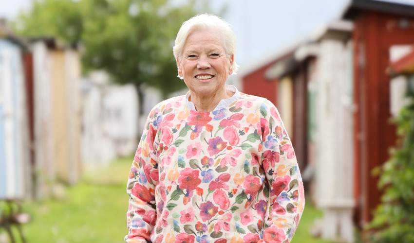 Pia står klädd i blommigt framför badhytter.