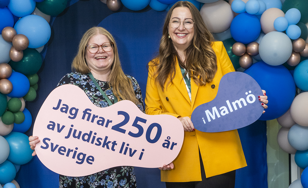 Två personer som står och håller skyltar framför ballonger. På skyltarna står " Jag firar 250 år av judiskt liv i Sverige. I Malmö ".