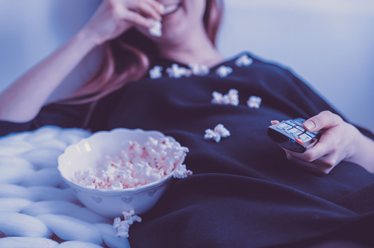 Skrattande kvinna tittar på film och äter popcorn.