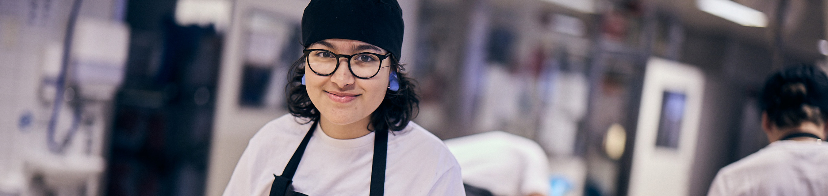 En leende elev med kockmössa,
glasögon och förkläde i bagerimiljö