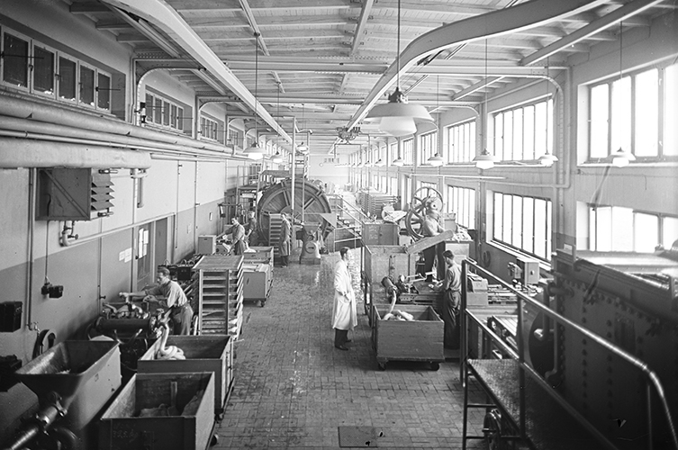 Äldre fotografi inuti fabriksbyggnaden, personer arbetar vid maskinerna.