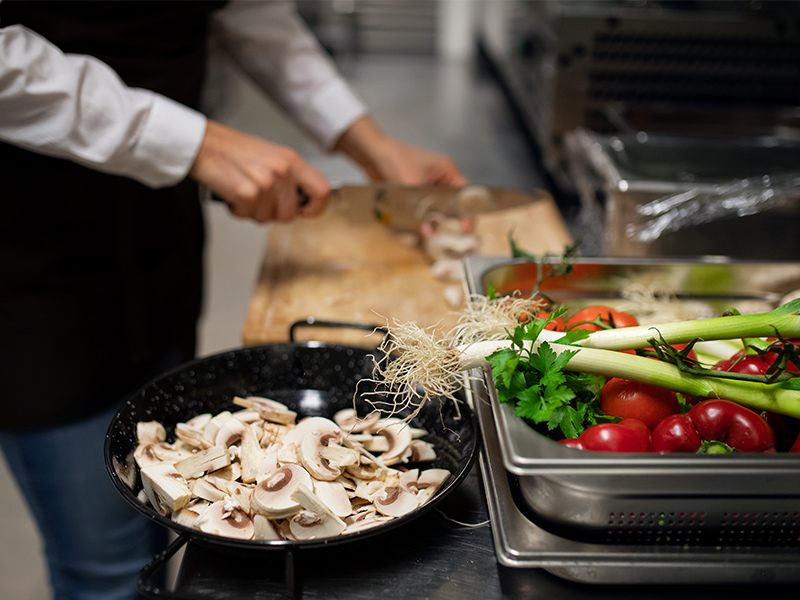 Medarbetare i
  restaurangkök skivar svamp och andra grönsaker.