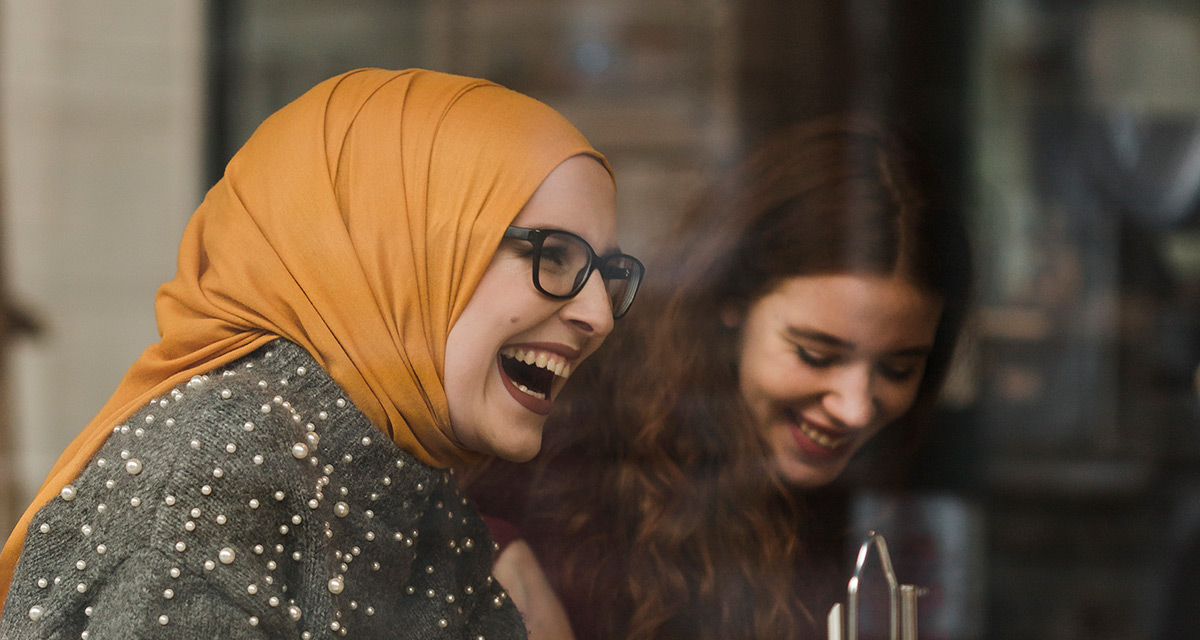En kvinna med glasögon och orange hijab har trevligt med vänner.