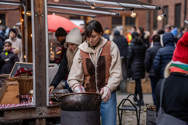 Fotografi på välbesökt marknad. En kvinna står och gör brända mandlar.