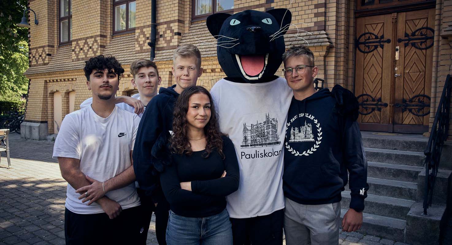 Fem elever i en gruppbild tillsammans med Pauliskolans maskot ute på skolgården.