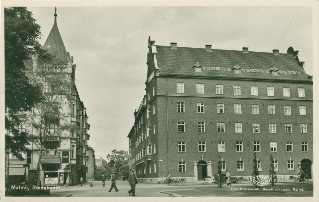 En svartvit stadsbild med en stor tegelbyggnad till höger.