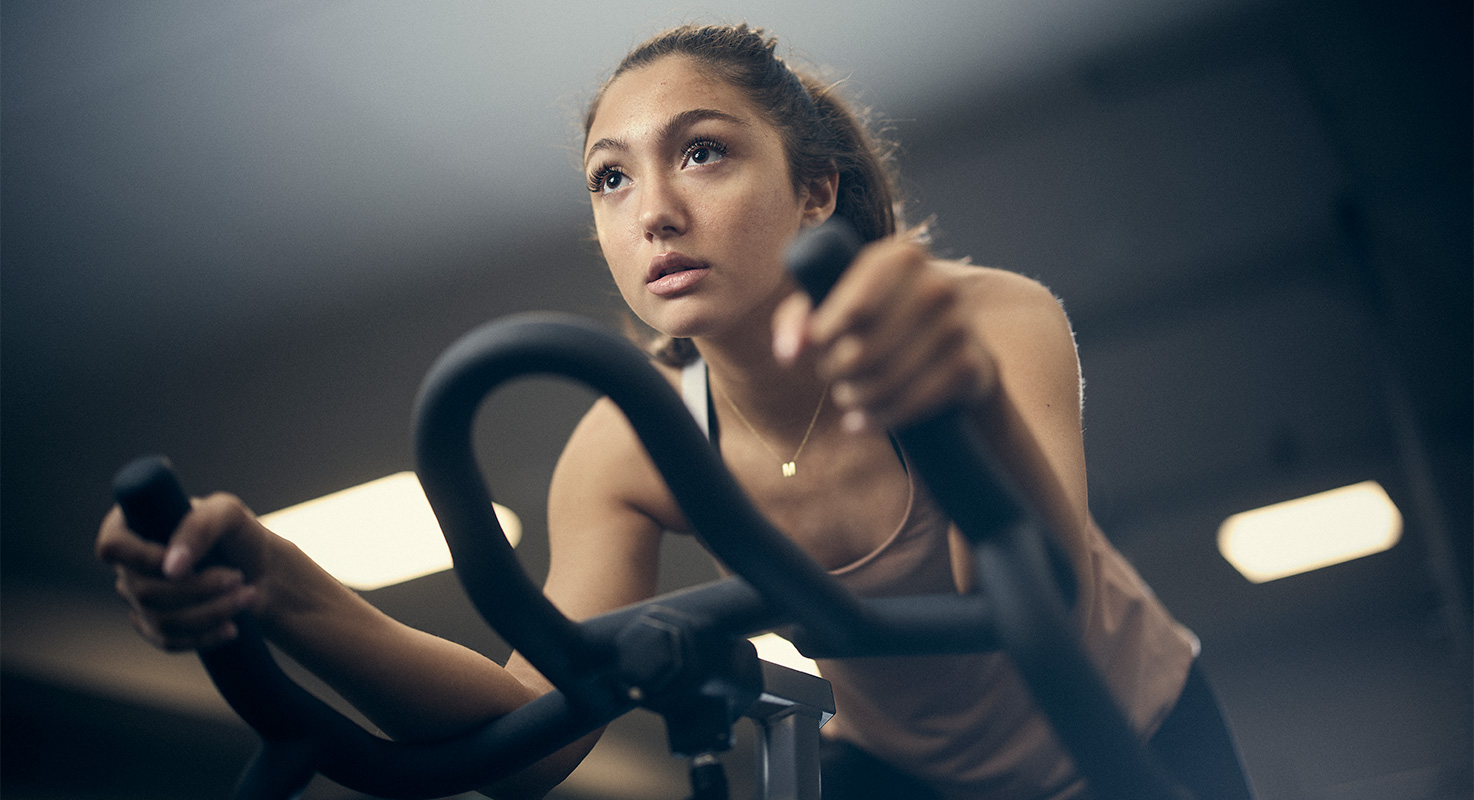 Tjej i skolans gym tränar på en spinningsmaskin.