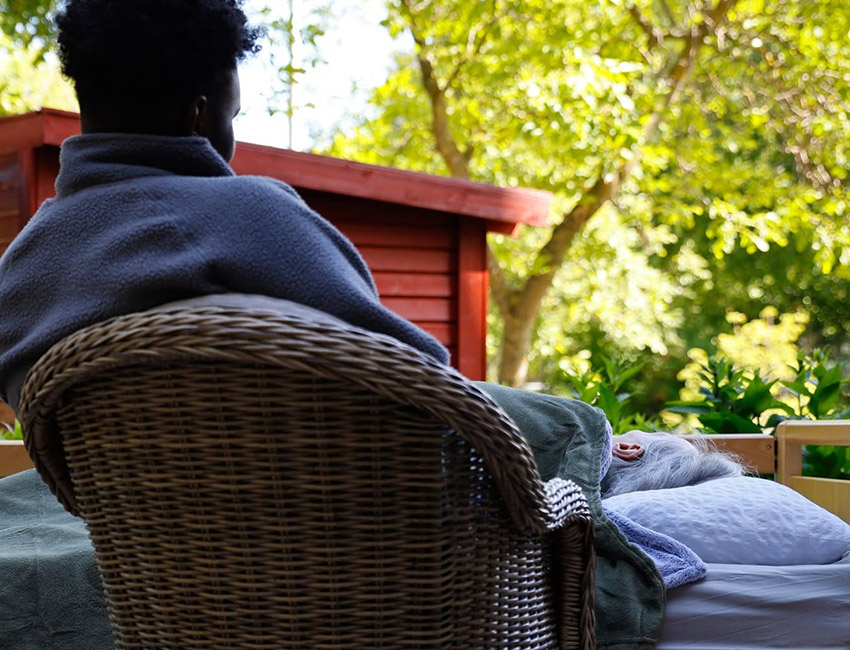 Personal sitter vid sidan om en säng där en boende vilar.