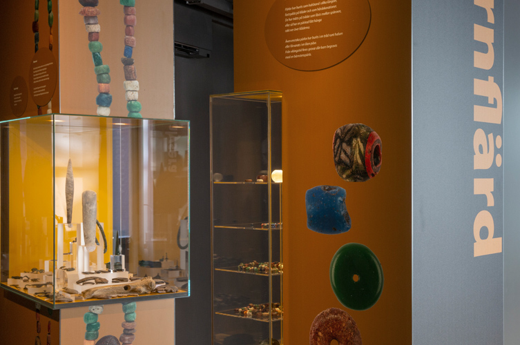 Bildspel med fotografier från utställningen. Färgstarkan väggar och glasmontrar med forntidssmycken, pärlor och annat pynt.