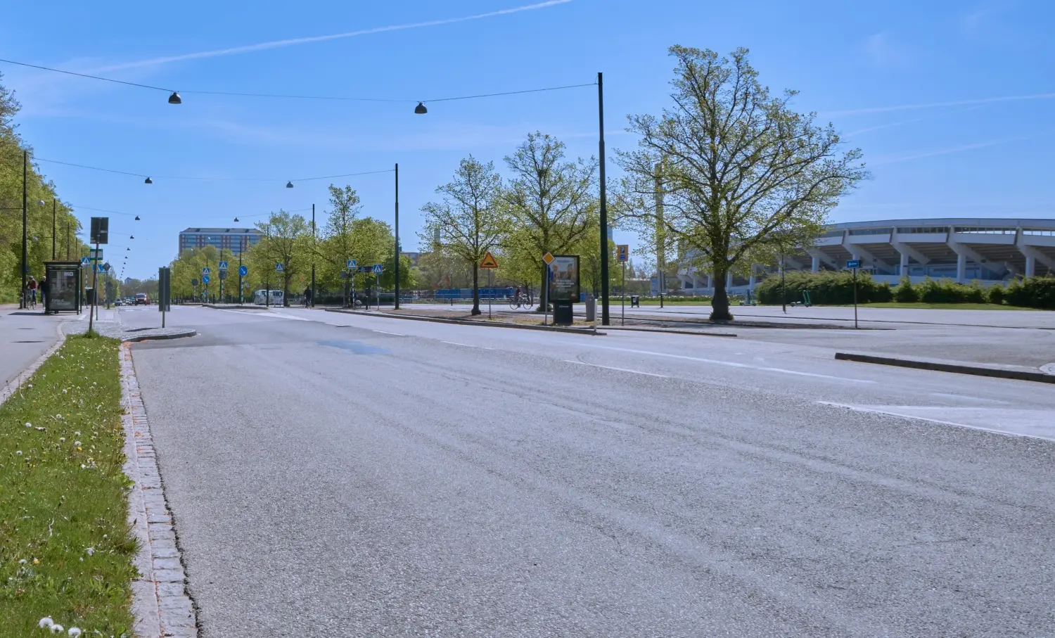 En bred gata kantad av träd. Malmö stadion ses i bakgrunden. 