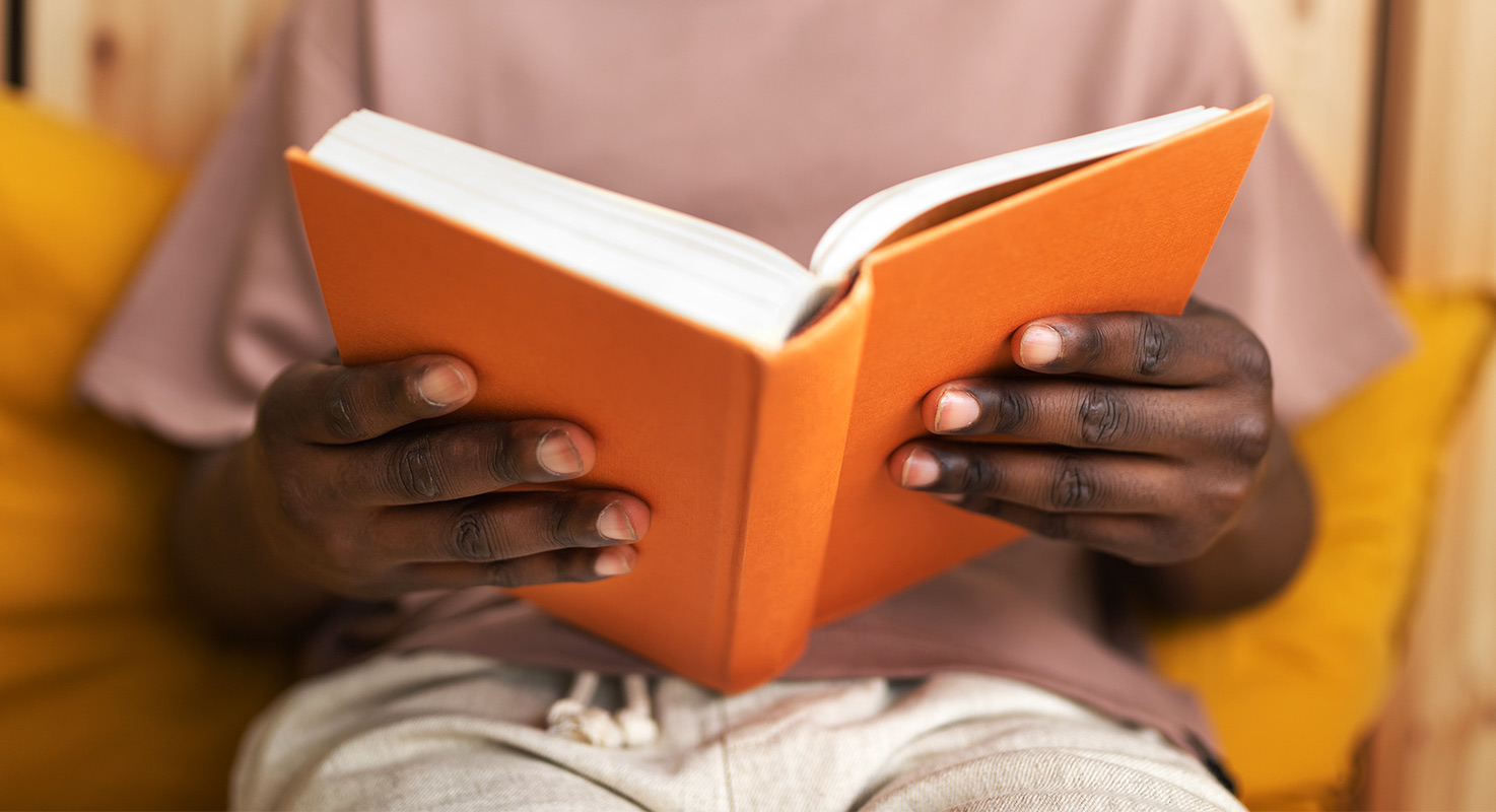 En person som tittar i en bok. Bokomslaget är i
orange färg.