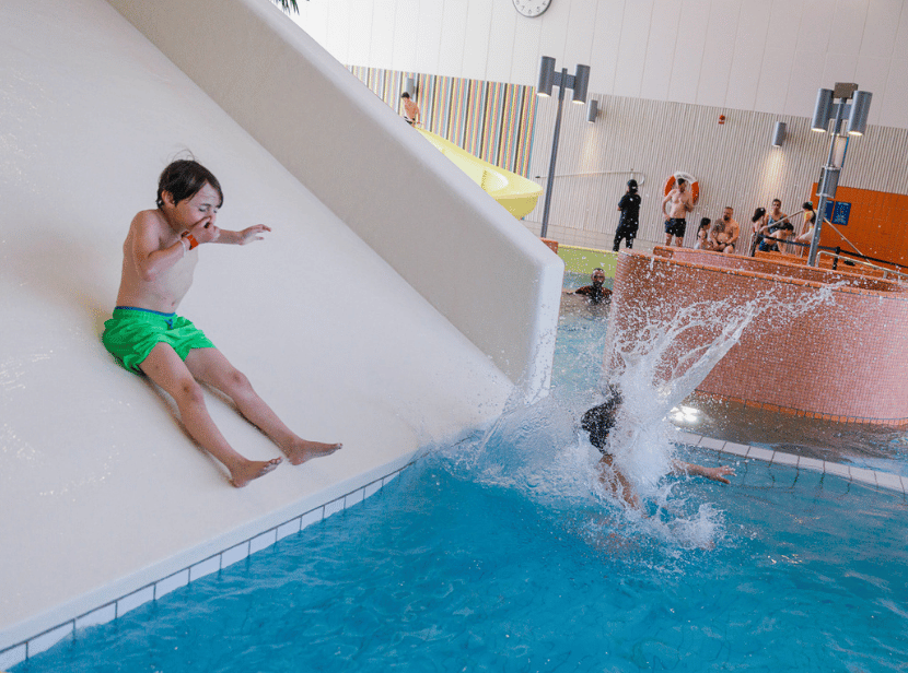 Hylliebadets maskotar Ella och Leif står vid bassängen Simmet och vinkar mot kameran.