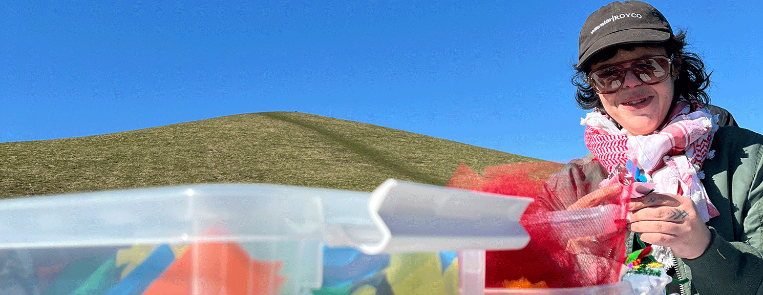 Kvinna pysslar utomhus, blå himmel och gröna kullar.