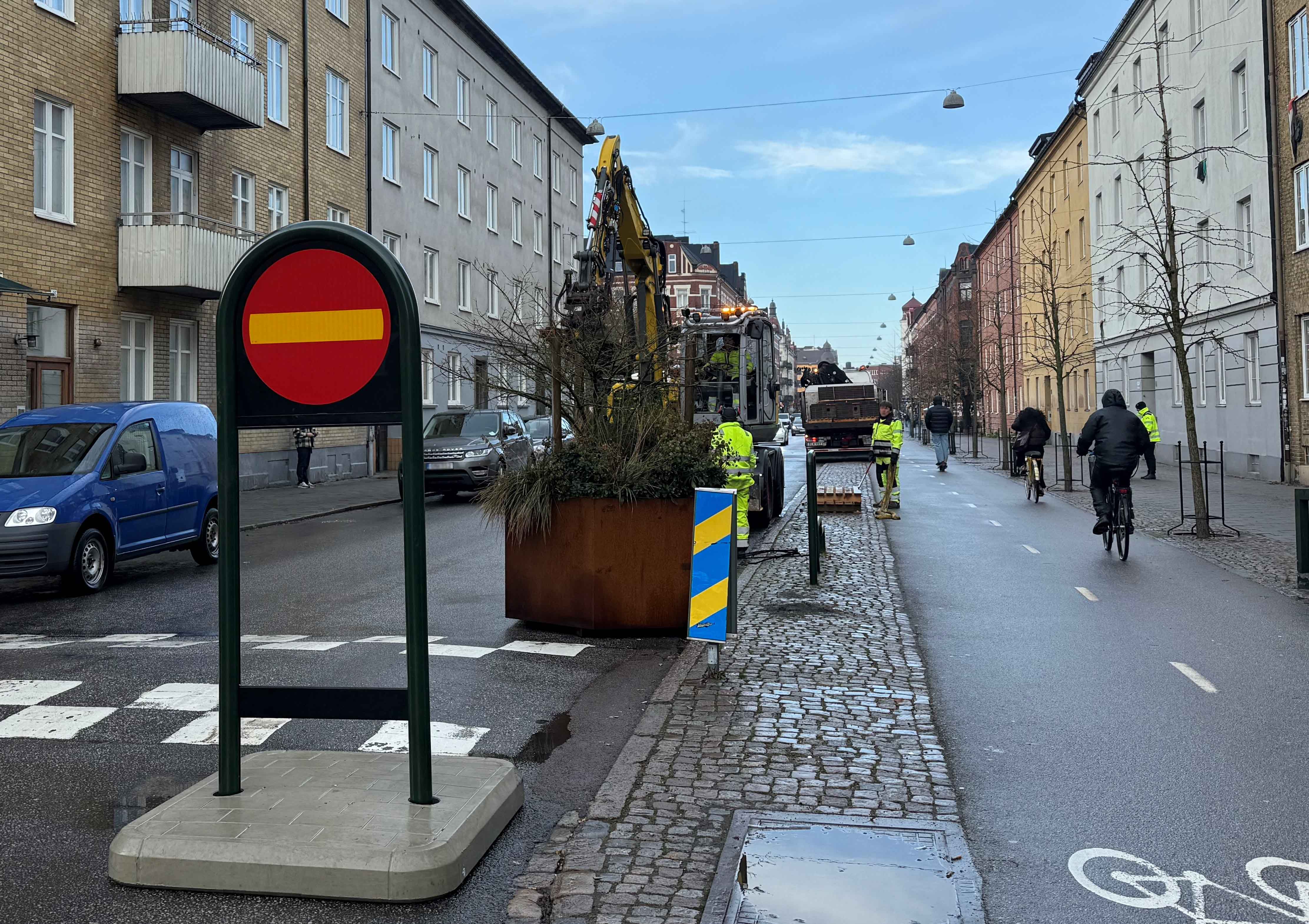 Ystadsgatan sett österifrån, i höjd med Falkenbergsgatan. Här finns trädplanteringar och vägmärke som visar att gatan är enkelriktad. Längs med gatan pågår trafiken, med bilister, cyklister och gående.