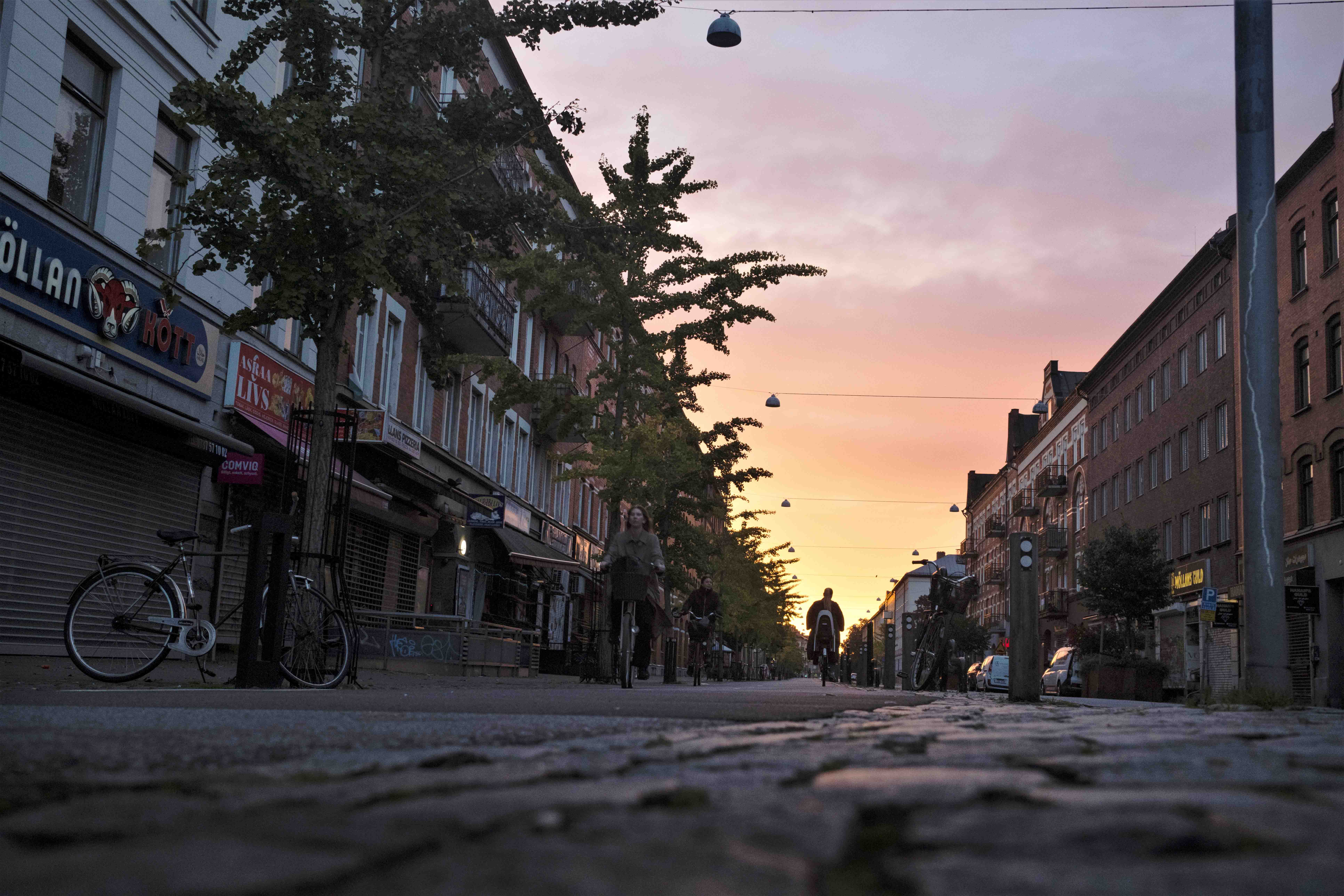 Cyklister cyklar på Ystadsgatans cykelbana i riktning mot Nobelvägen. Det är skymning och rosa himmel, en fin oktoberkväll på Möllevången.
