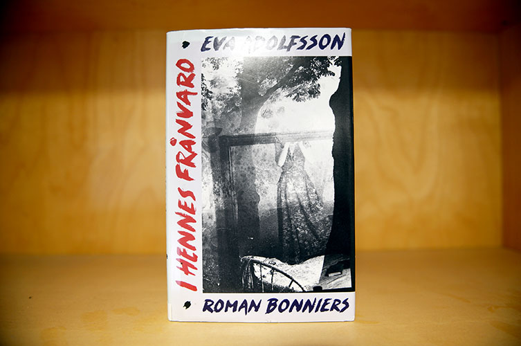 Omslag till boken "I hennes frånvaro" med svartvitt diffust fotografi av kvinna och träd.