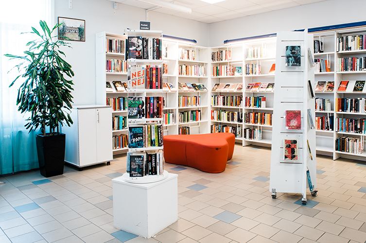 Interiör på Bellevuegårdsbiblioteket som visar del av vuxenavdelningen. Med bokhyllor och bekväm sittplats.