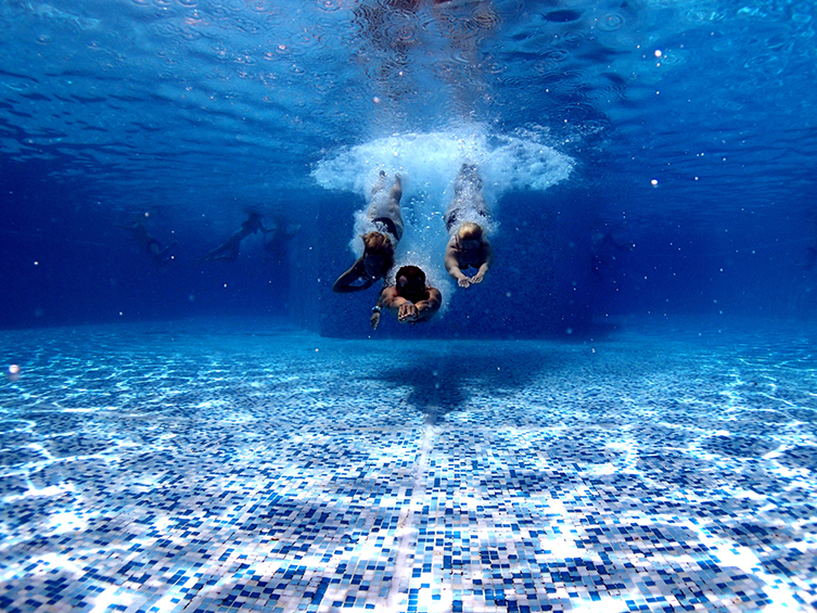 Tre personer som dyker ner i en simbassäng. 
