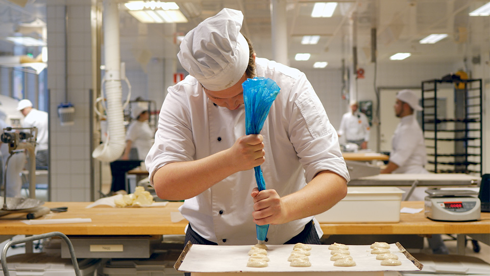 Bagare spritsar upp kakor med hjälp av en spritstyll på en bakplåt