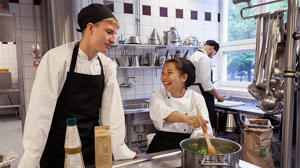 Två elever, en kille och en tjej, lagar mat
tillsammans. Tjejen ler.