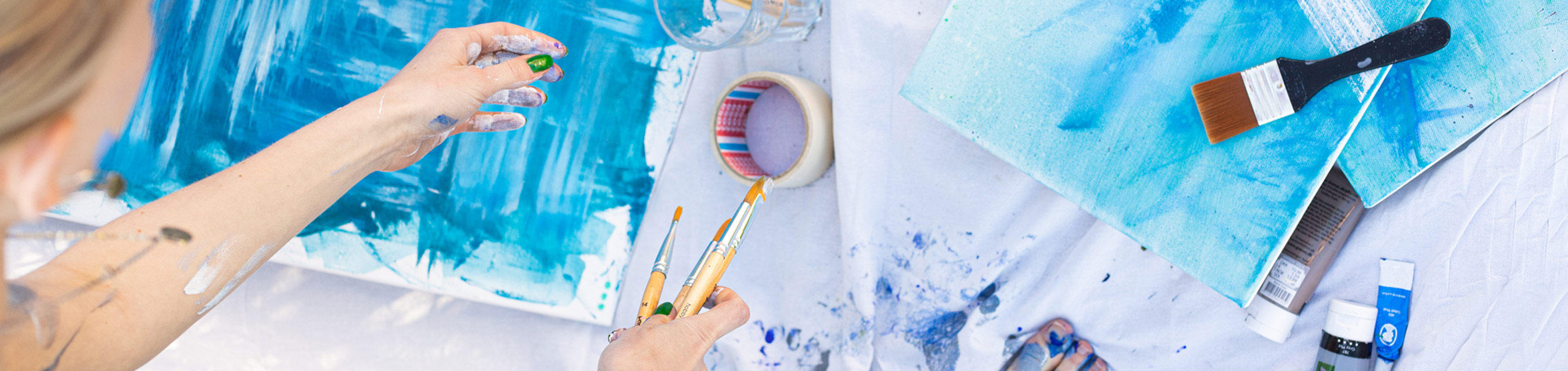 En elev med målarduk, penslar och färg som är igång att måla i blåa toner