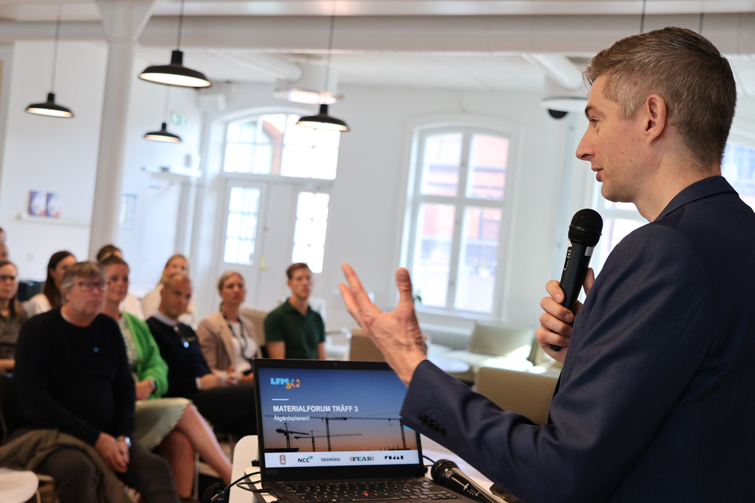 En man i kavaj från LFM30 står och pratar framför en publik.