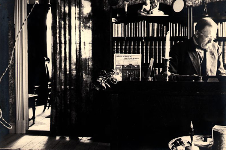 En rumsinteriör från Axel och Gretha Cronquists hem i Högsby i Småland 1923. Axel Cronquist sitter vid ett skrivbord framför en bokhylla. Fotograf okänd/Malmö Museer.
