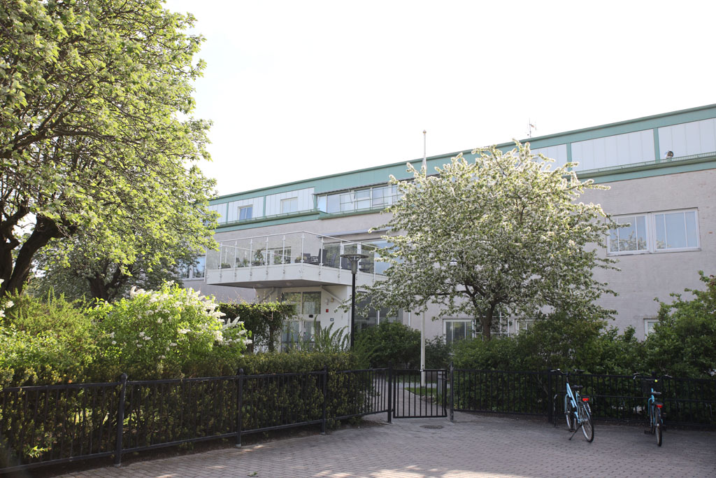 Husets
fasad går i ljusgrönt och vitt och är omringad av buskar och träd. 