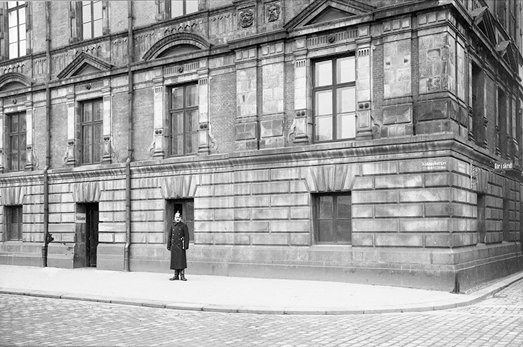 Svartvitt fotografi på polisman framför stor byggnad.