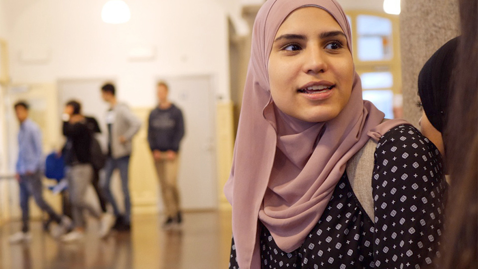 Elev i rosa slöja och svart tröja med mönster i skolans
entréhall.