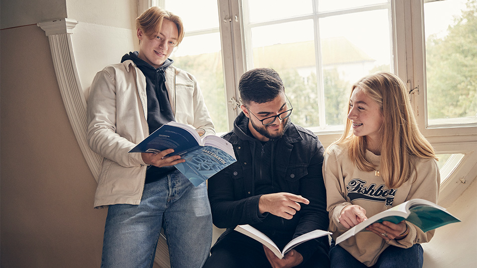 Tre elever som sitter i fönstret och samtalar
över sina böcker.