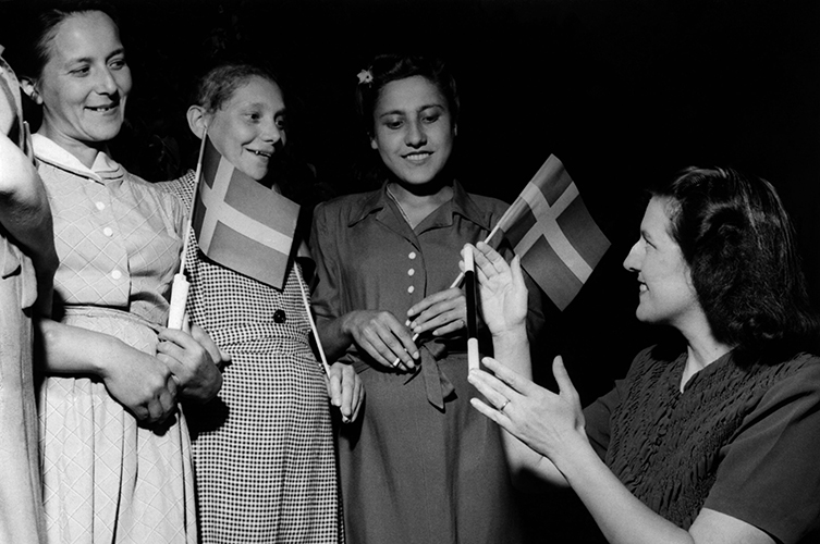 Äldre foto på fyra kvinnor, en av dem håller en svensk flagga i handen.