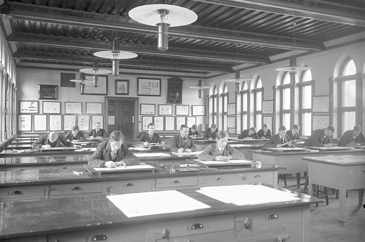 Äldre svartvitt foto på undervisningssal med ett 15-tal mån i kostym.