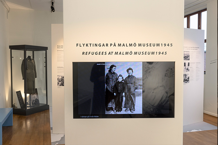 Utställningslokalen med montrar och en stor skärm som visar film.