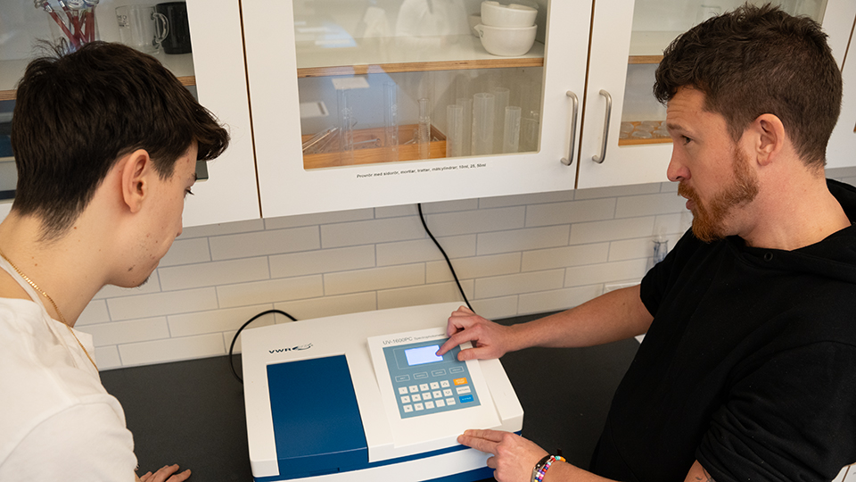 En elev och en lärare i en laborationssal. Läraren pekar på displayen på en apparat. 