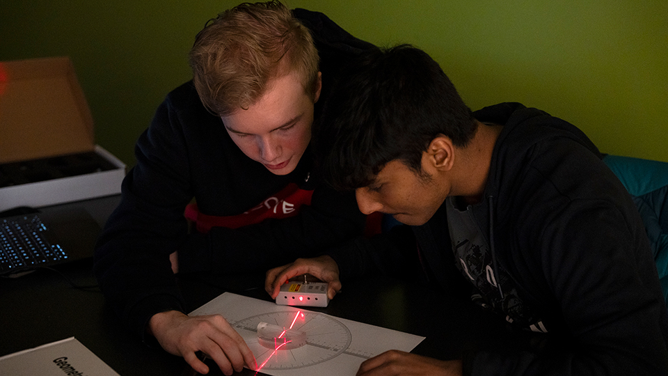 Två elever tittar på en röd ljusstråle och mäter något.