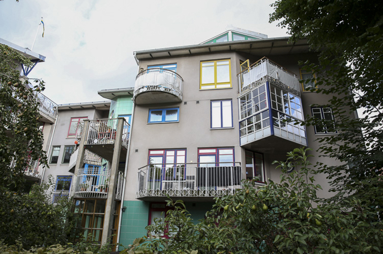 Fotografi på fasaden till huset Bo 100. Huset har balkonger och fönster i flera olika färger och former.