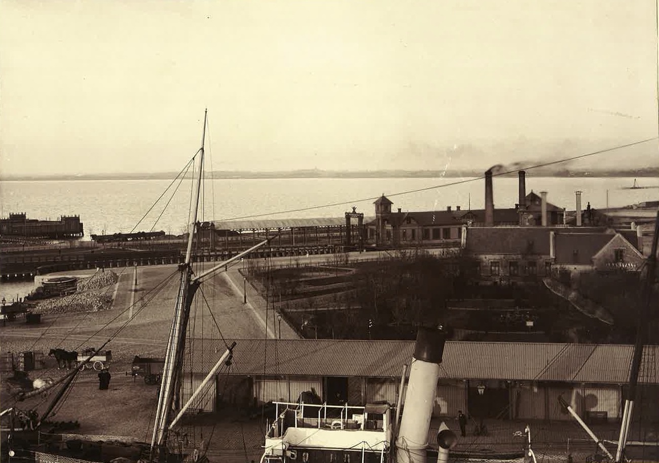 Ångbåtsbron längst ut på Östra Kajgatan (Skeppsbron)
tillkom 1879-81 och ångfärjestationen med anslutande järnvägsspår (Malmö F) först 1895. Till vänster syns det första
kallbadhuset.
Till höger om ångfärjestationen ses
varmbadhuset med två skorstenar.