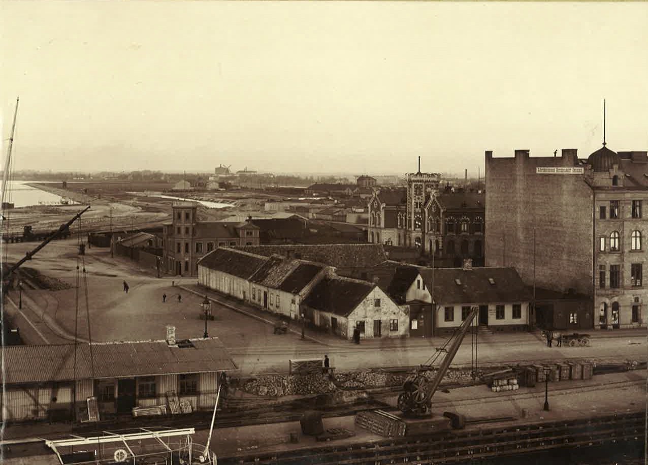 Östra Kajgatan (Skeppsbron) i hörnet av
nuvarande Hans Michelsensgatan där Kolgahuset numera finns. Tornet
bakom de låga husen hör till lotsstationen. Nästan hundra år senare byggdes Öresundshuset på samma tomt, där
lotsen och Sjöfartsverket sitter idag. Till vänster bakom det högre huset ligger Navigationsskolan.  