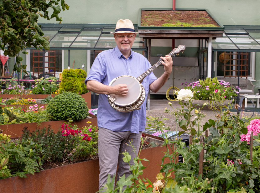 Olof håller i sin banjo där han står i mötesplatsens gröna trädgård.