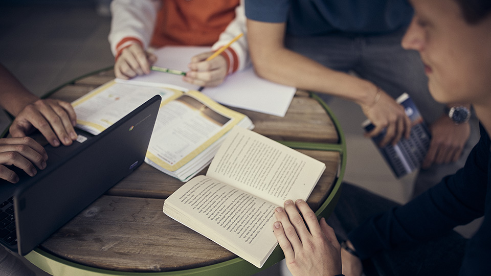 fyra ungdomar sitter och studerar vid ett bord. En jobbar på dator, de andra läser och skriver.