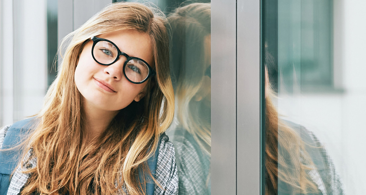 En ung tjej med glasögon står lutad mot en
glasvägg.