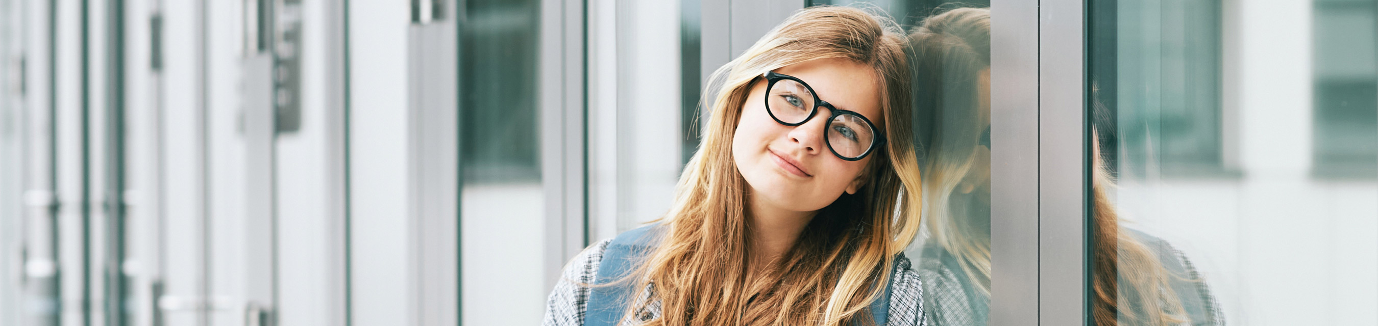 En ung tjej med glasögon står lutad mot en
glasvägg.