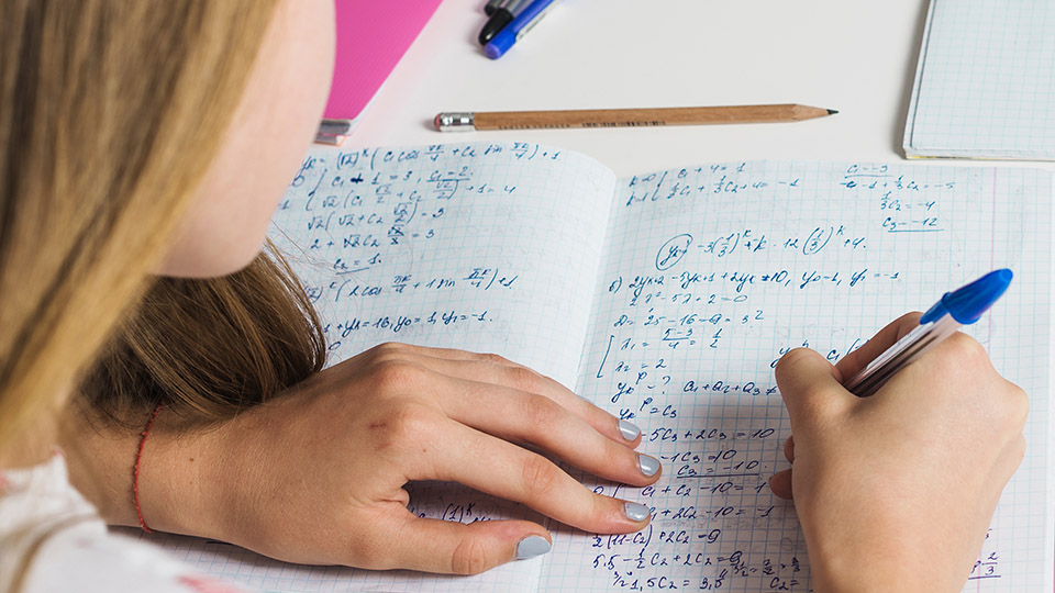 Närbild på en långhårig person som skriver
matematiska formler i ett skrivhäfte.