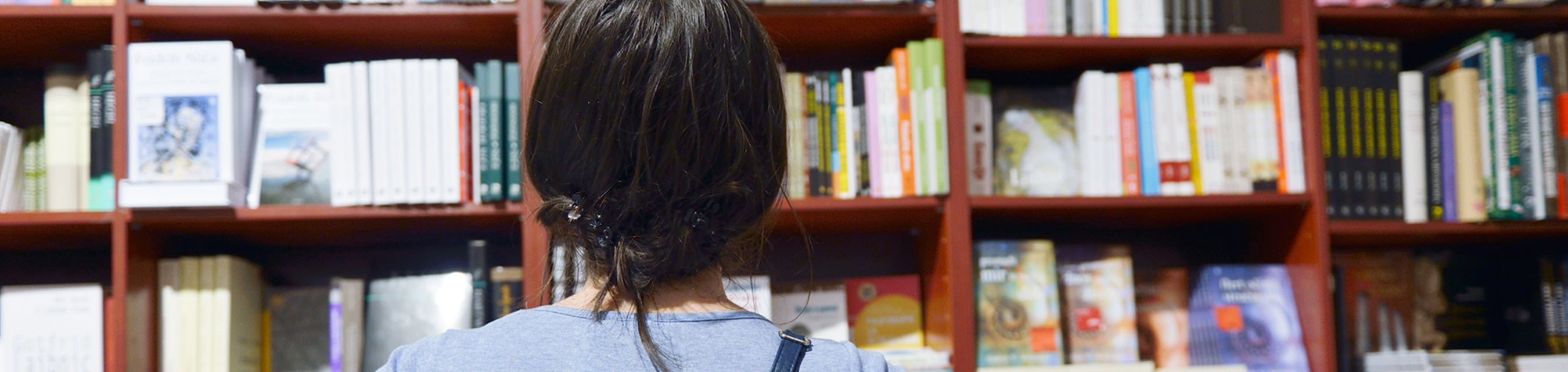 Kvinna funderar över vilken bok hon ska välja i en bokhylla med böcker.