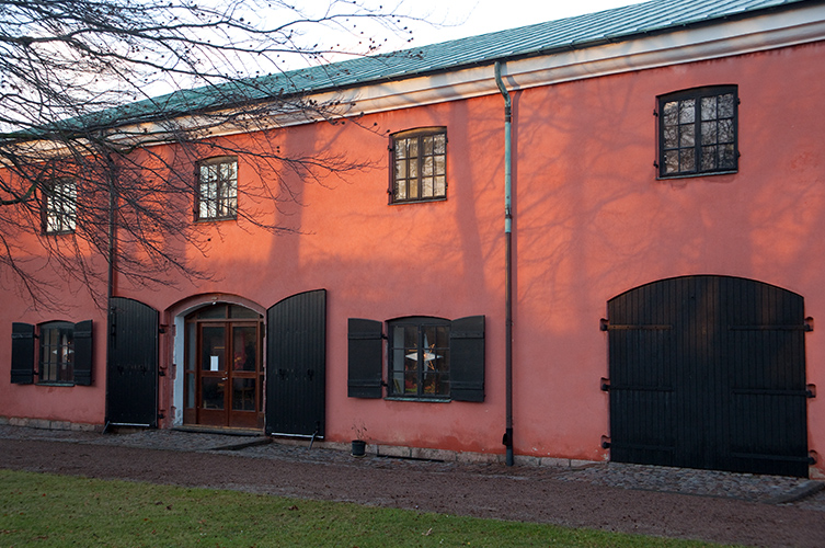 Fotografi på Kommendanthuset, ett hus i röd puts med svarta fönsterluckor och dörrportar. 