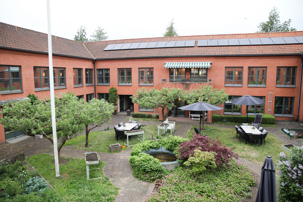 En lummig och grönskande innerträdgård som omringas av ett
rött tvåvåningshus.